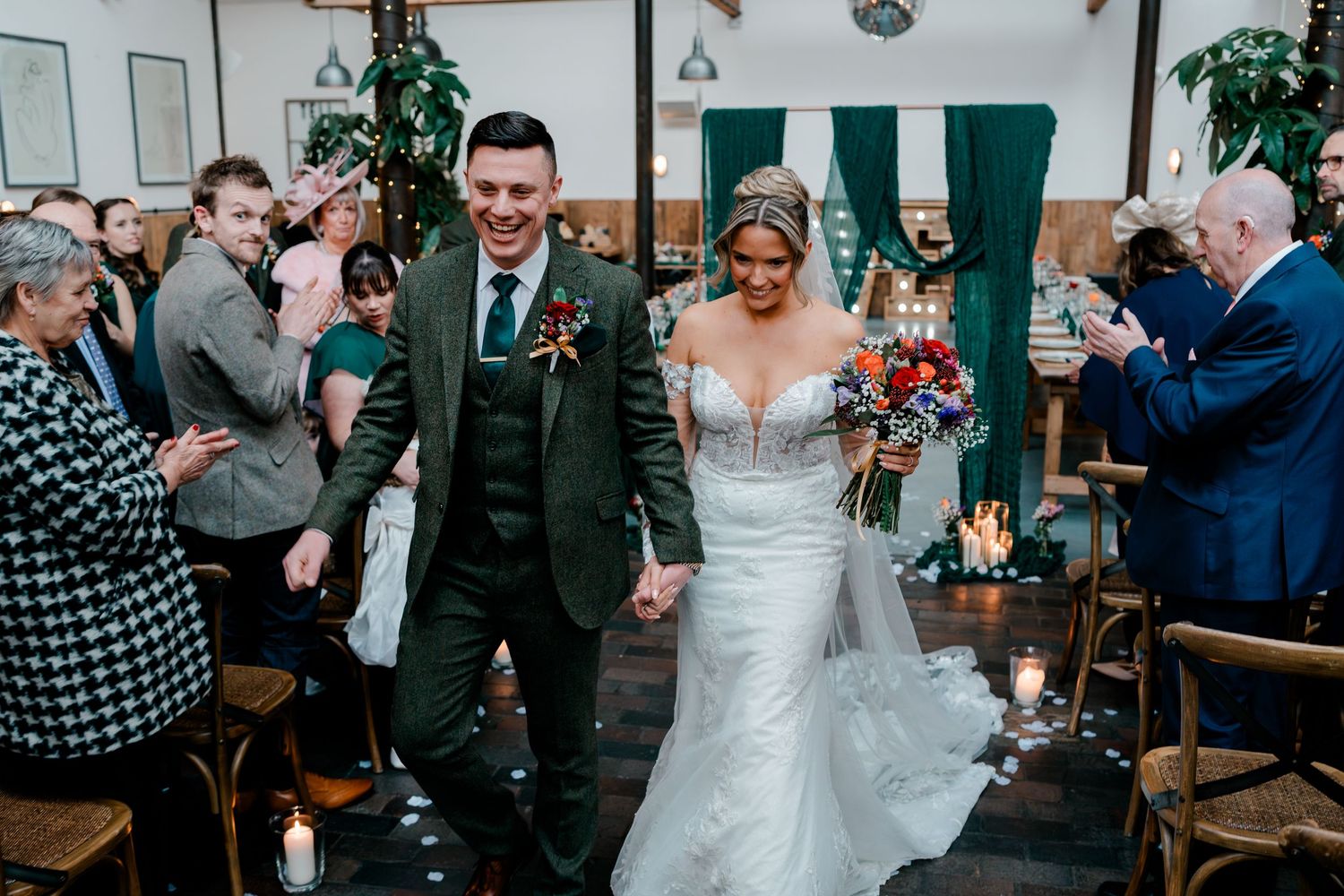 Newlyweds walk back down the aisle as guests celebrate with applause at wedding reception.