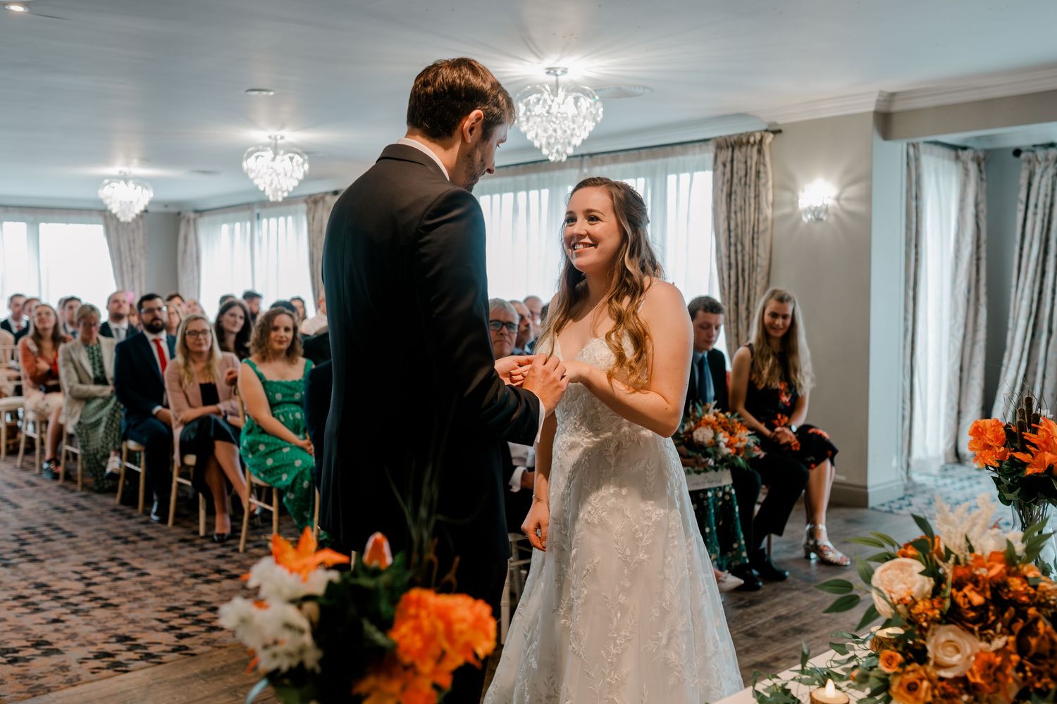 A wedding ceremony collage showing elegant venue details with chandeliers and orange floral decorations.