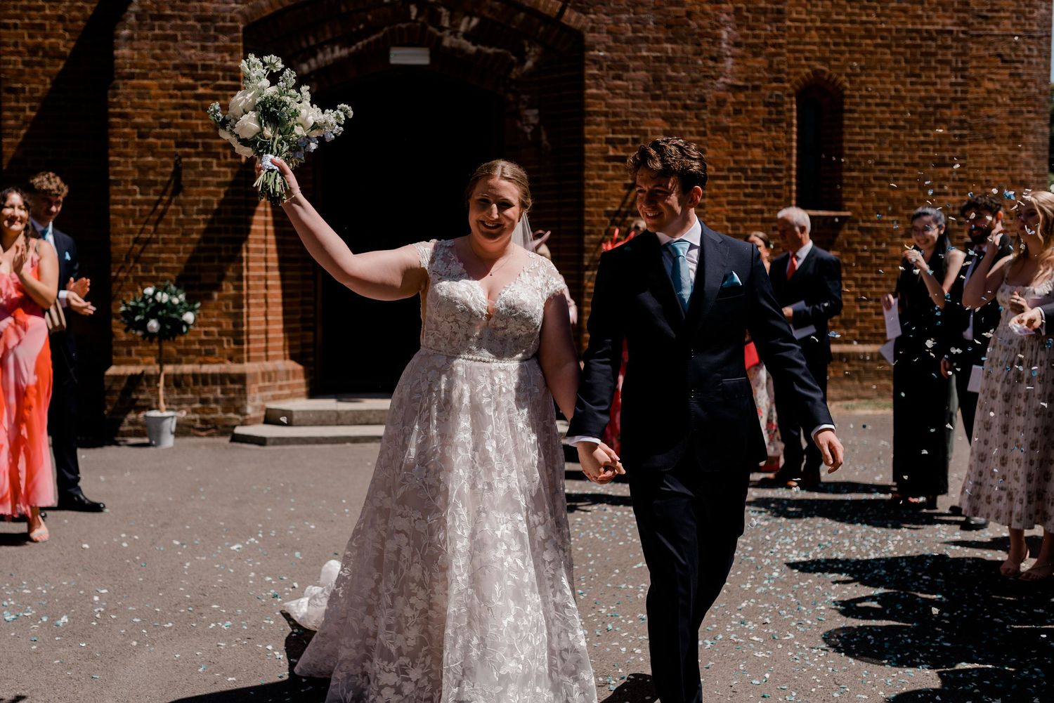 Smiling newlyweds walking down church aisle while guests shower them with white flower petals during recessional.