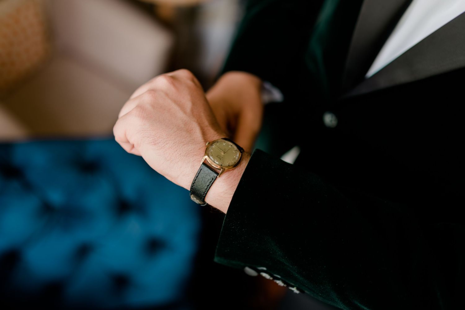 Close-up of a groom checking a gold watch on his wrist in a dark suit jacket.