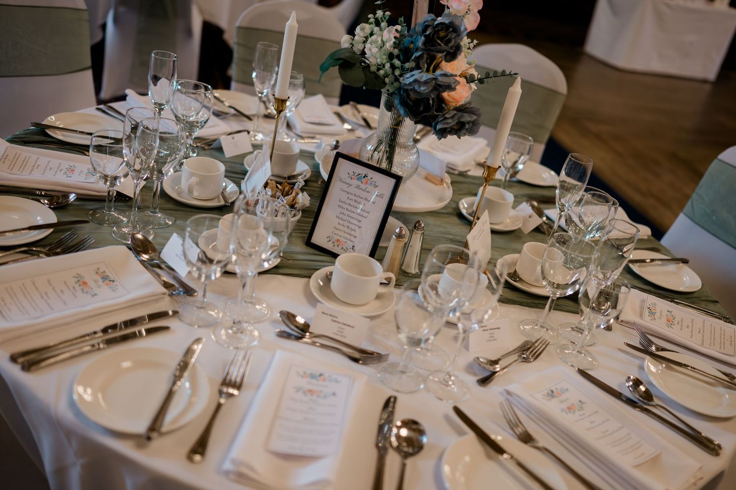 Elegantly set wedding reception table with white linens, glassware, and floral centerpieces.
