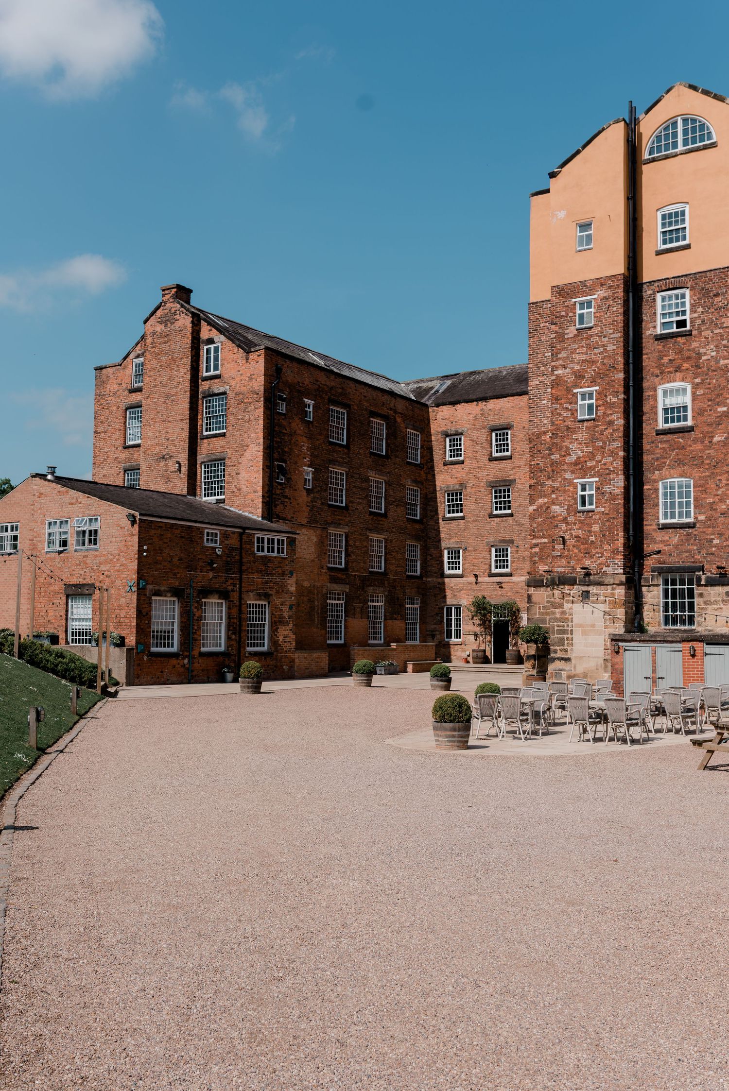 Grand red brick mill wedding venue courtyard with gravel ground and outdoor seating on a bright sunny day.
