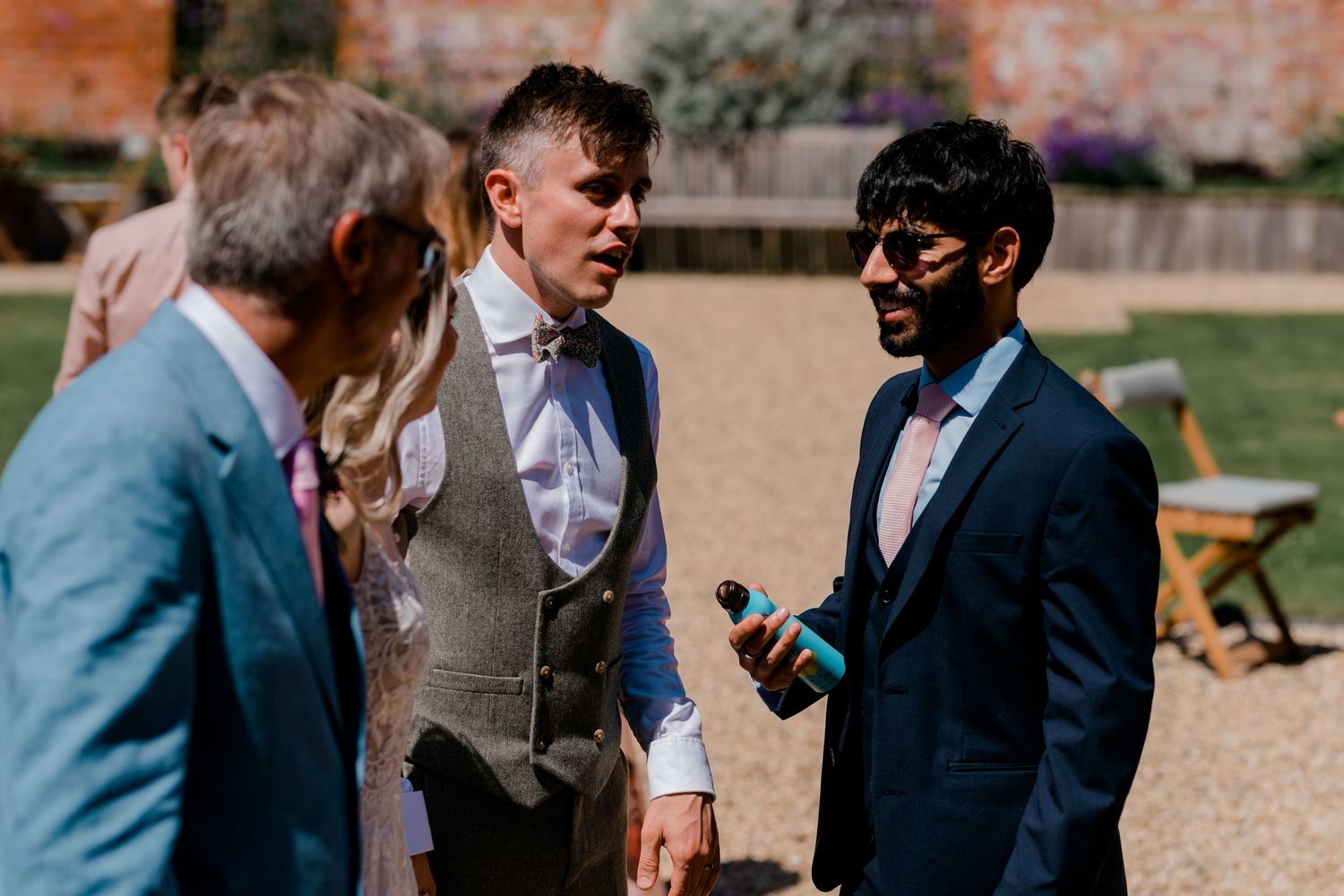 Wedding guests mingle and socialize outdoors in formal attire during a garden reception.
