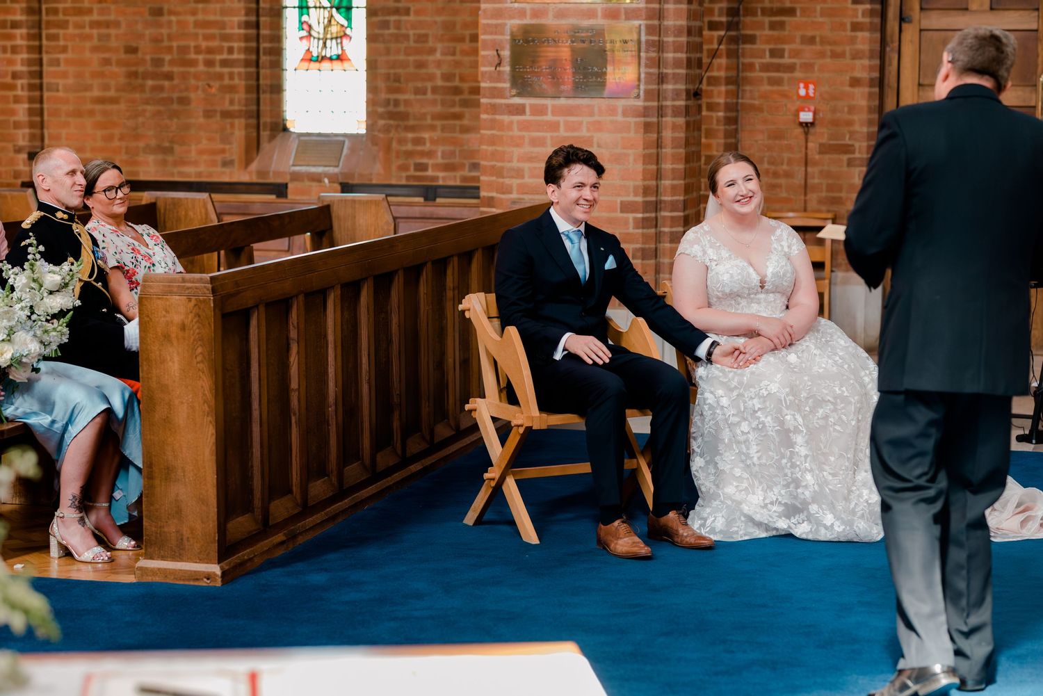 Wedding ceremony in a traditional brick church with wooden pews and blue carpet aisle.