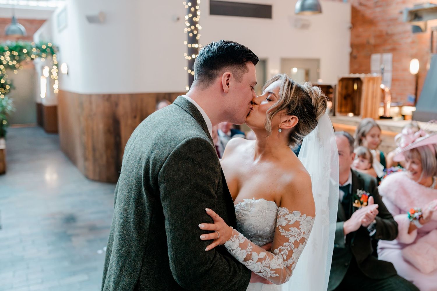 Newlyweds share their first kiss as husband and wife during wedding ceremony at a rustic indoor venue.