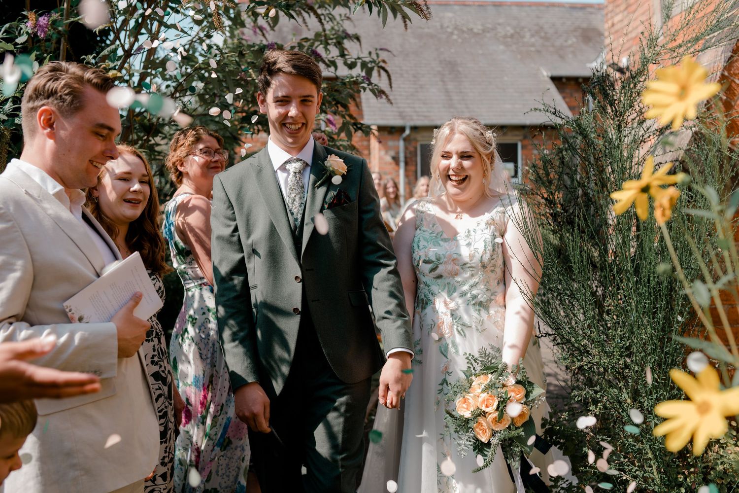 Wedding celebration in a sunny garden with guests throwing confetti during festivities.