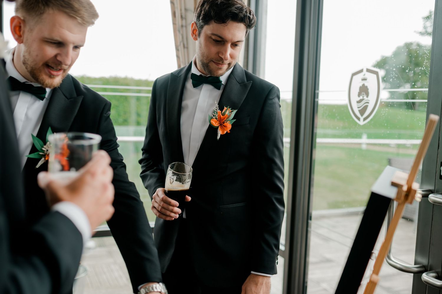 A group of groomsmen in black tuxedos toast with champagne glasses at a wedding celebration.