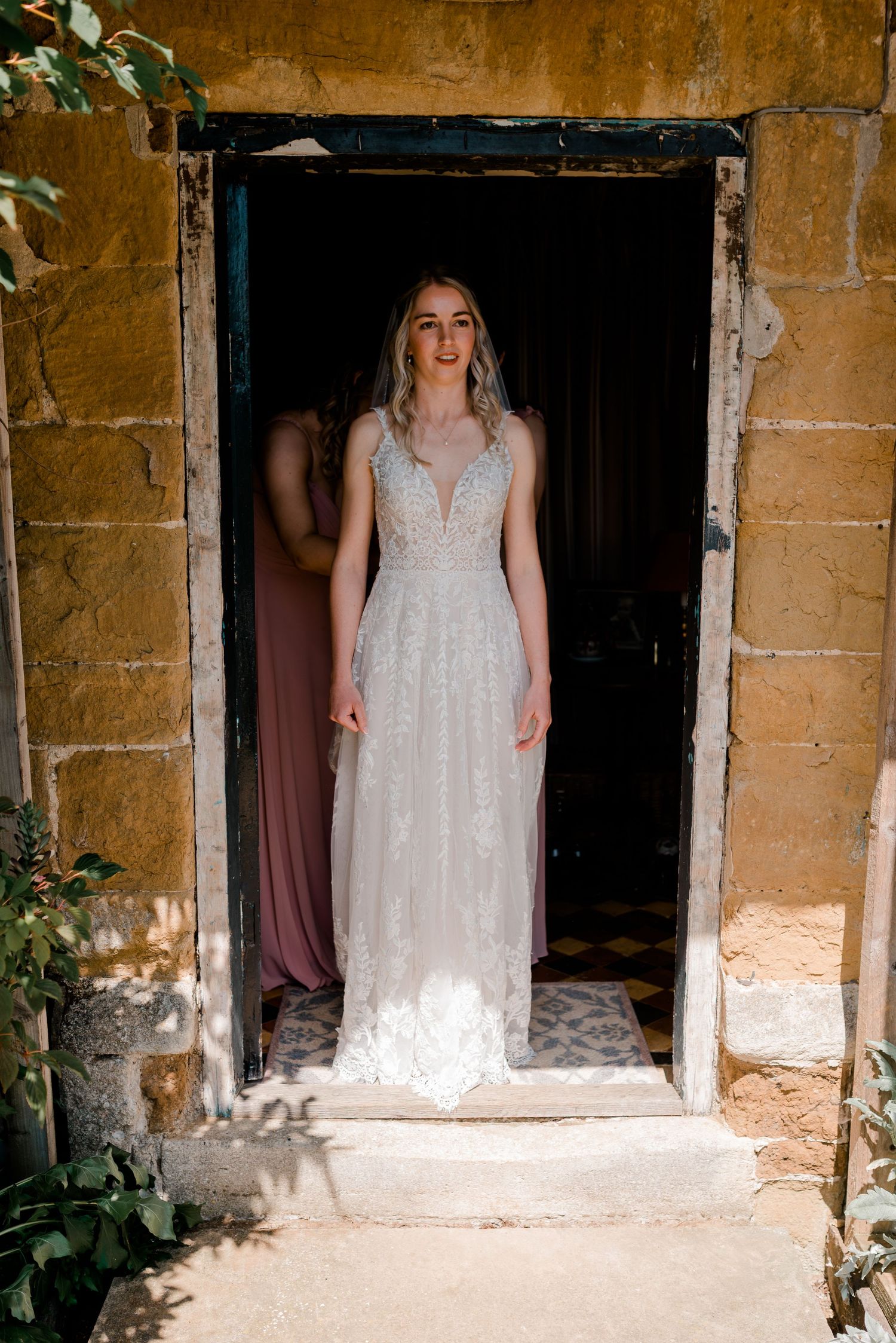 Elegant white lace wedding dress with plunging neckline photographed in rustic stone doorway.