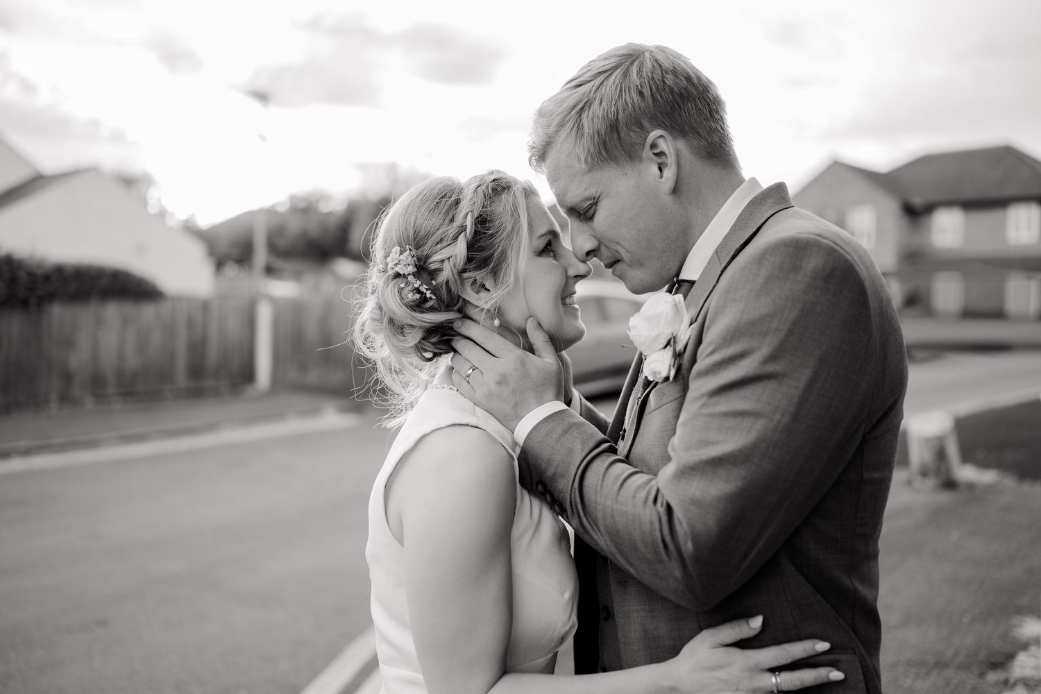 Black and white wedding photo of bride and groom sharing a romantic moment outdoors on a residential street.