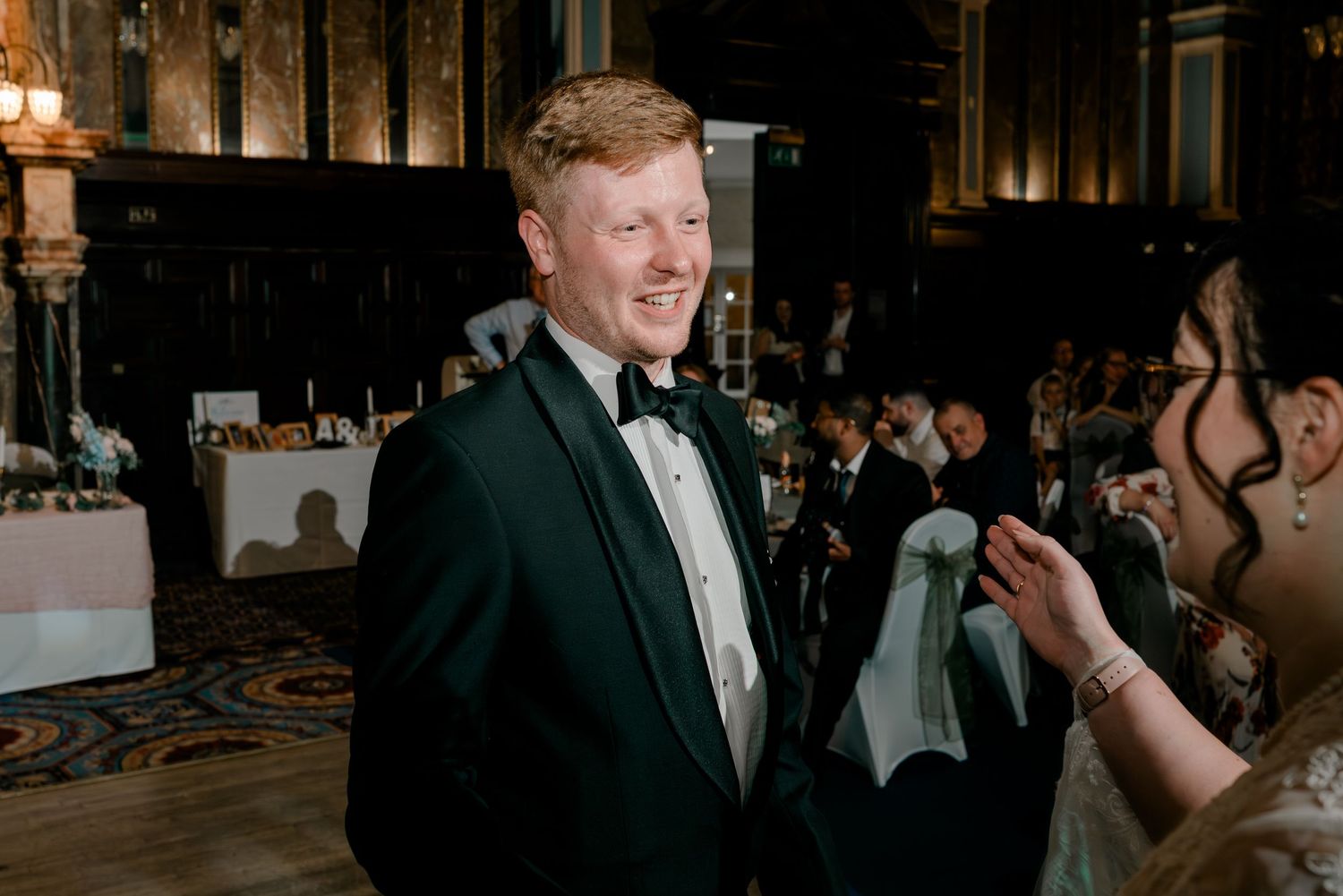 Smiling groom in green tuxedo at wedding reception in grand ballroom.