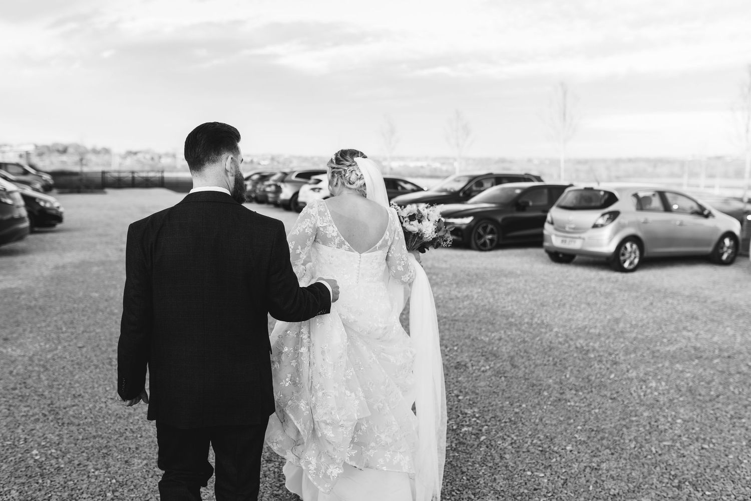 Black and white photo of newlyweds walking in a parking area.