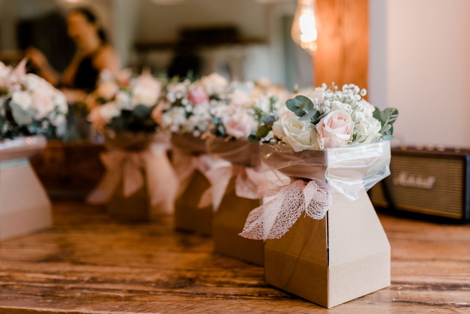 Small white favor boxes with delicate lace bows arranged on rustic wooden surface create an elegant wedding display.