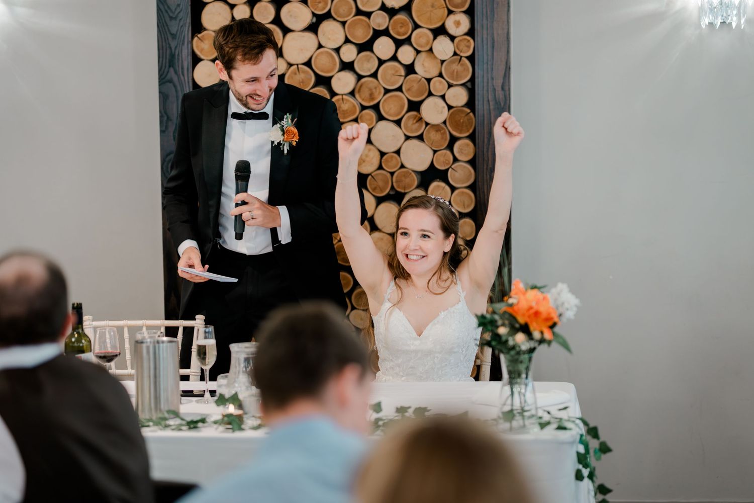 Wedding reception guests raise champagne glasses in a toast during a celebration at a rustic venue with wood decor.