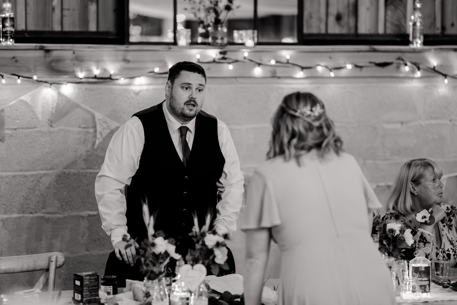 A wedding reception scene with fairy lights and table settings as guests interact during the celebration.