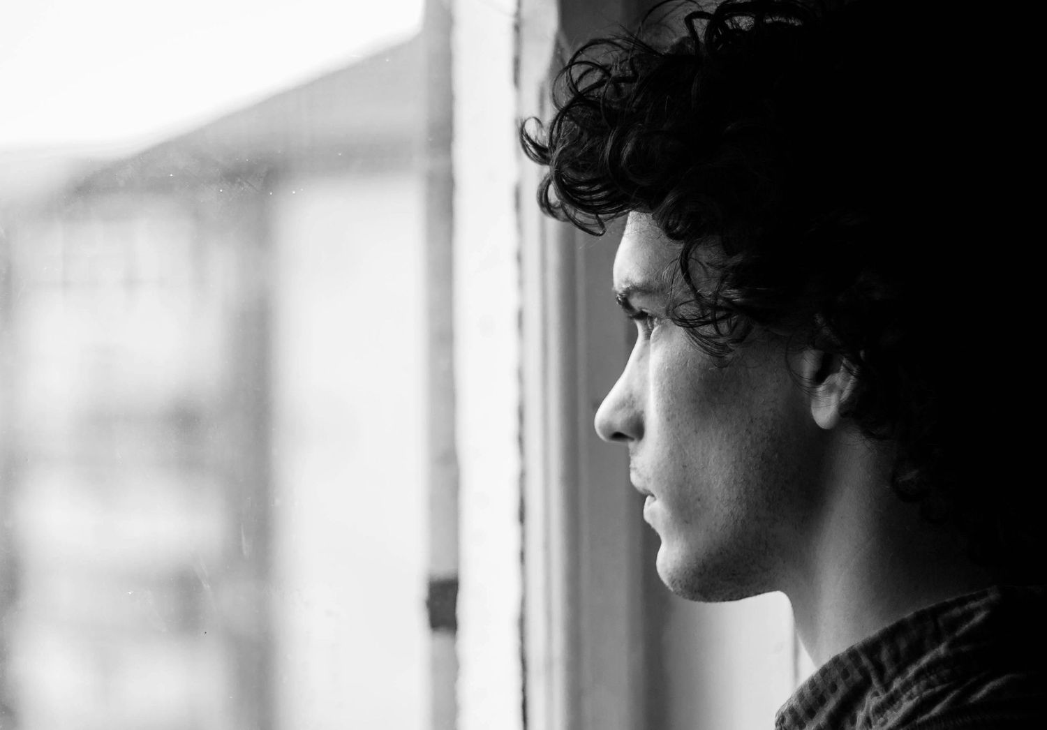 Artistic black and white profile portrait showing contemplative gaze through window light.