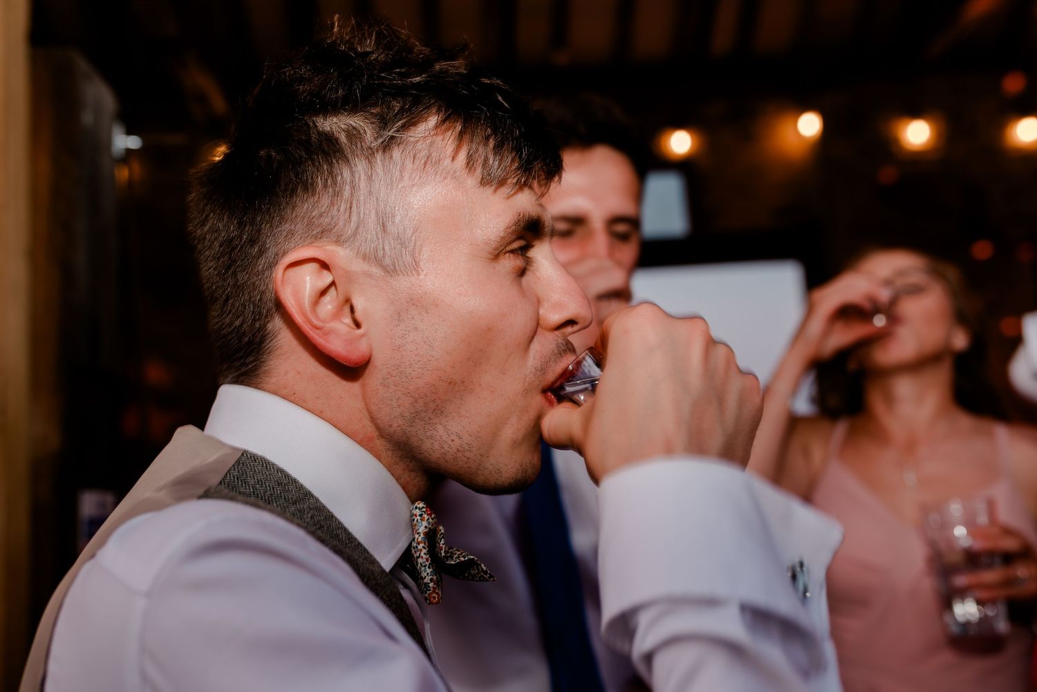Wedding reception guests dancing and celebrating under warm indoor lighting.
