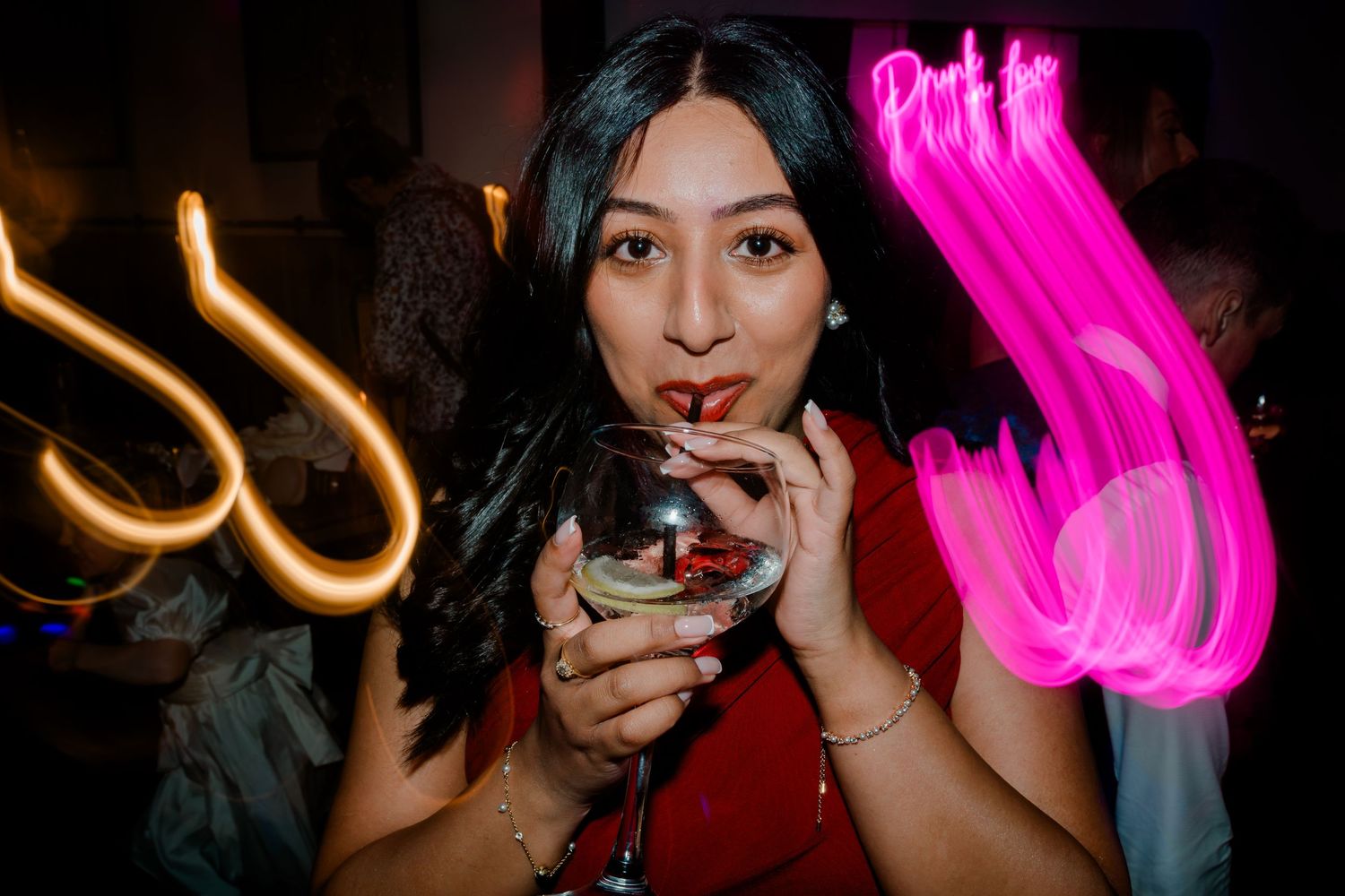 Woman sipping a cocktail with colorful neon light trails at a wedding party.