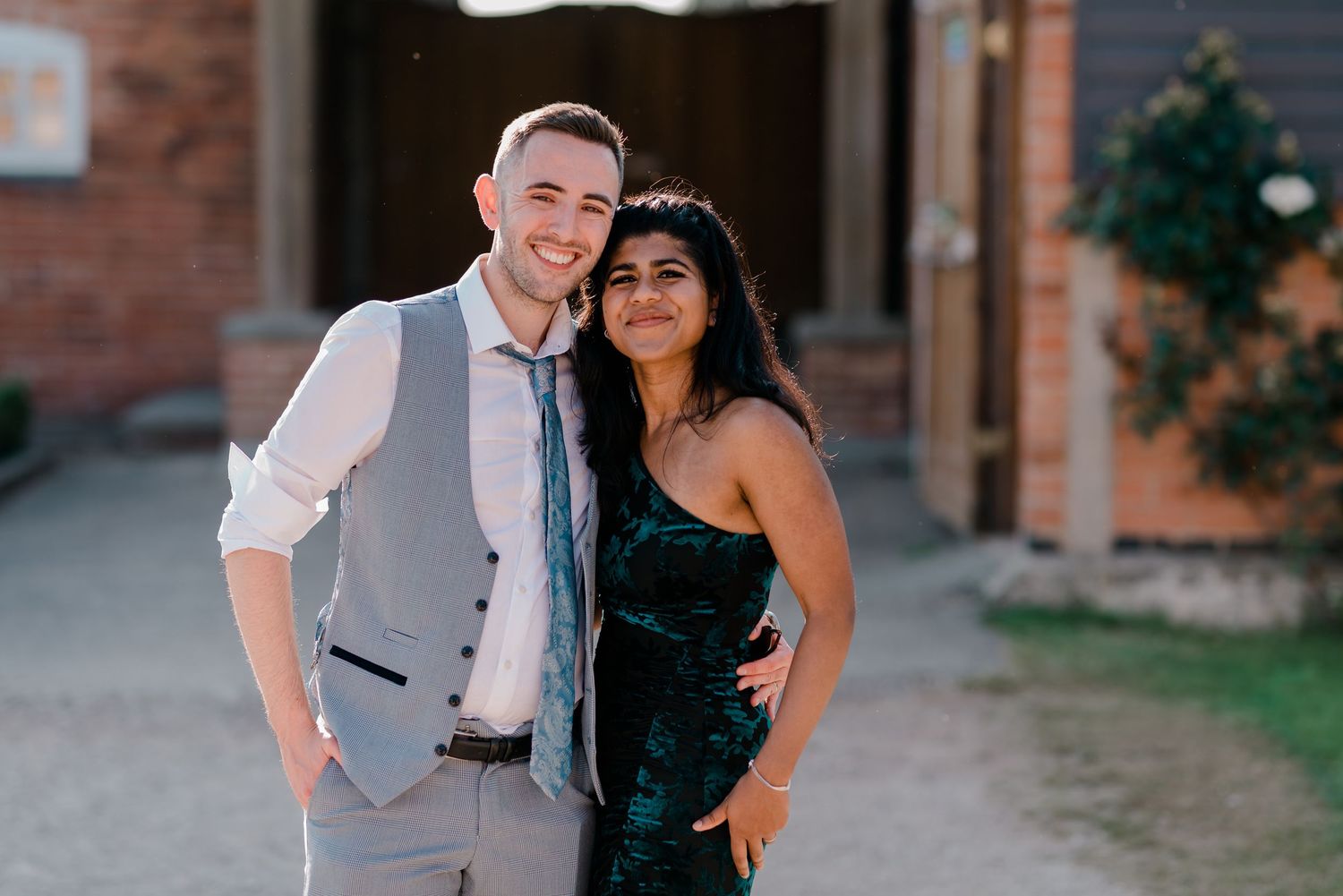 Couple shares romantic moments during outdoor photo session against brick building backdrop.