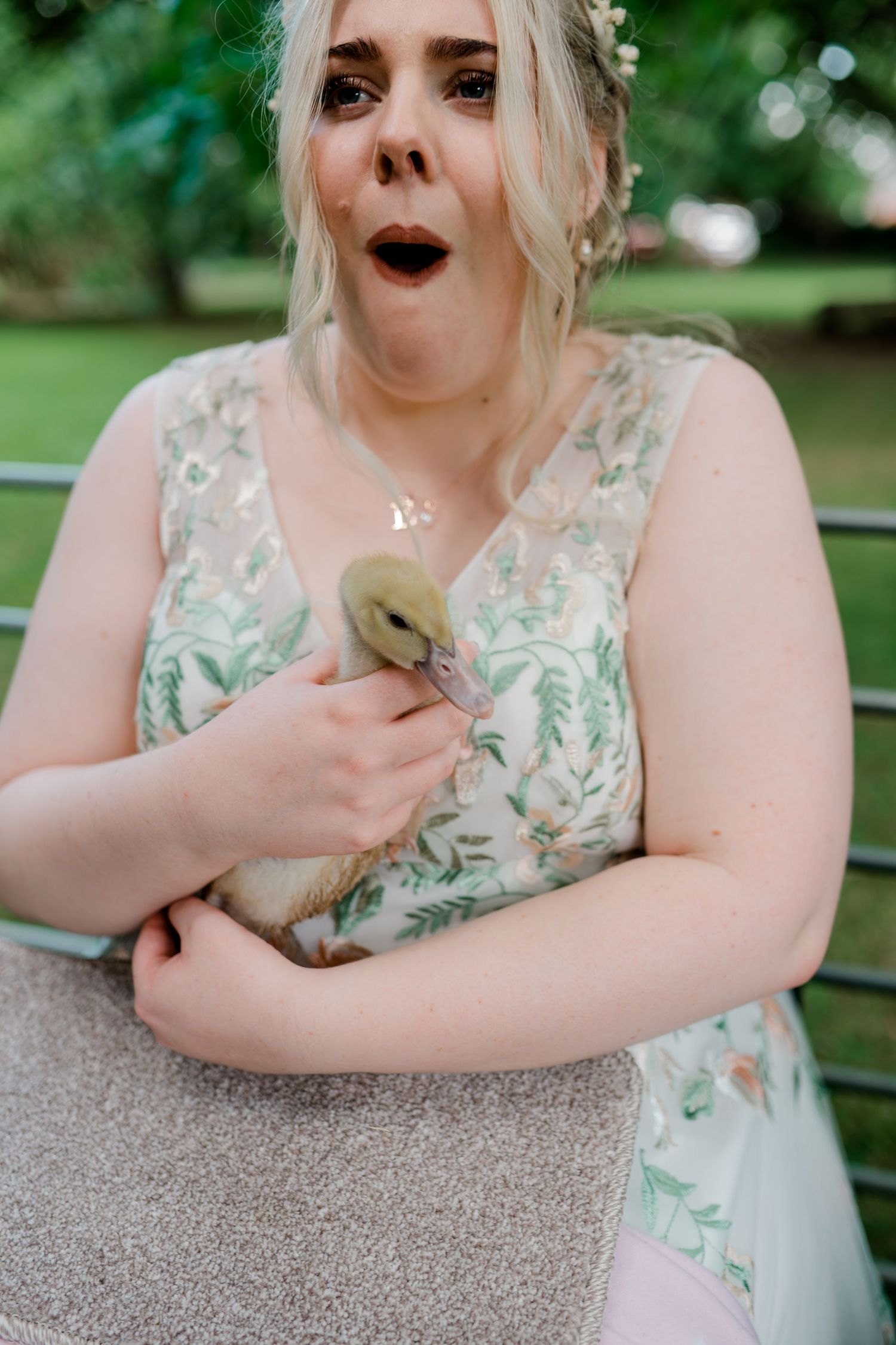A person in a floral dress reacts with surprise and delight while sitting at an outdoor table.
