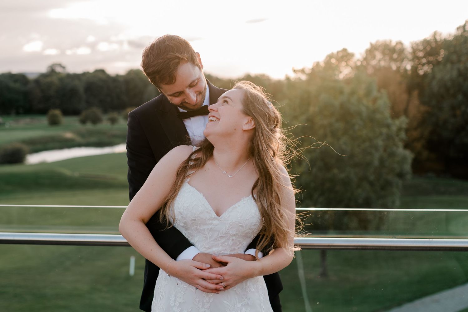 Bride and groom share a romantic sunset moment on a balcony overlooking a golf course.