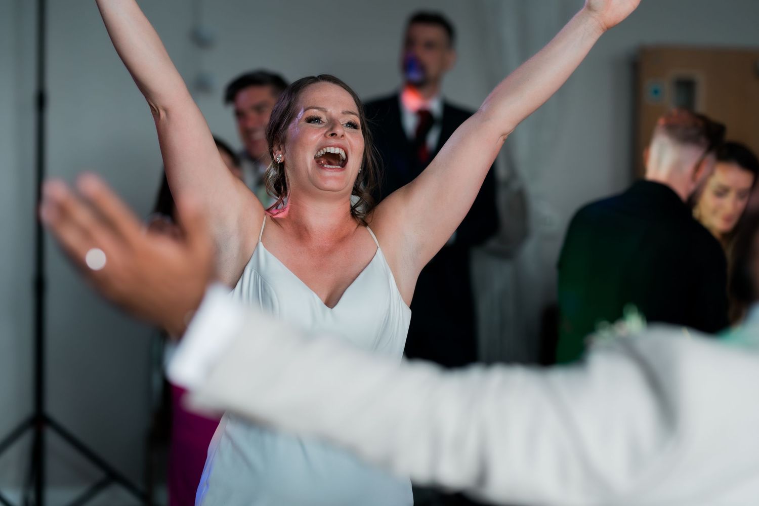 Joyful bride with arms raised celebrating on the dance floor at wedding reception.