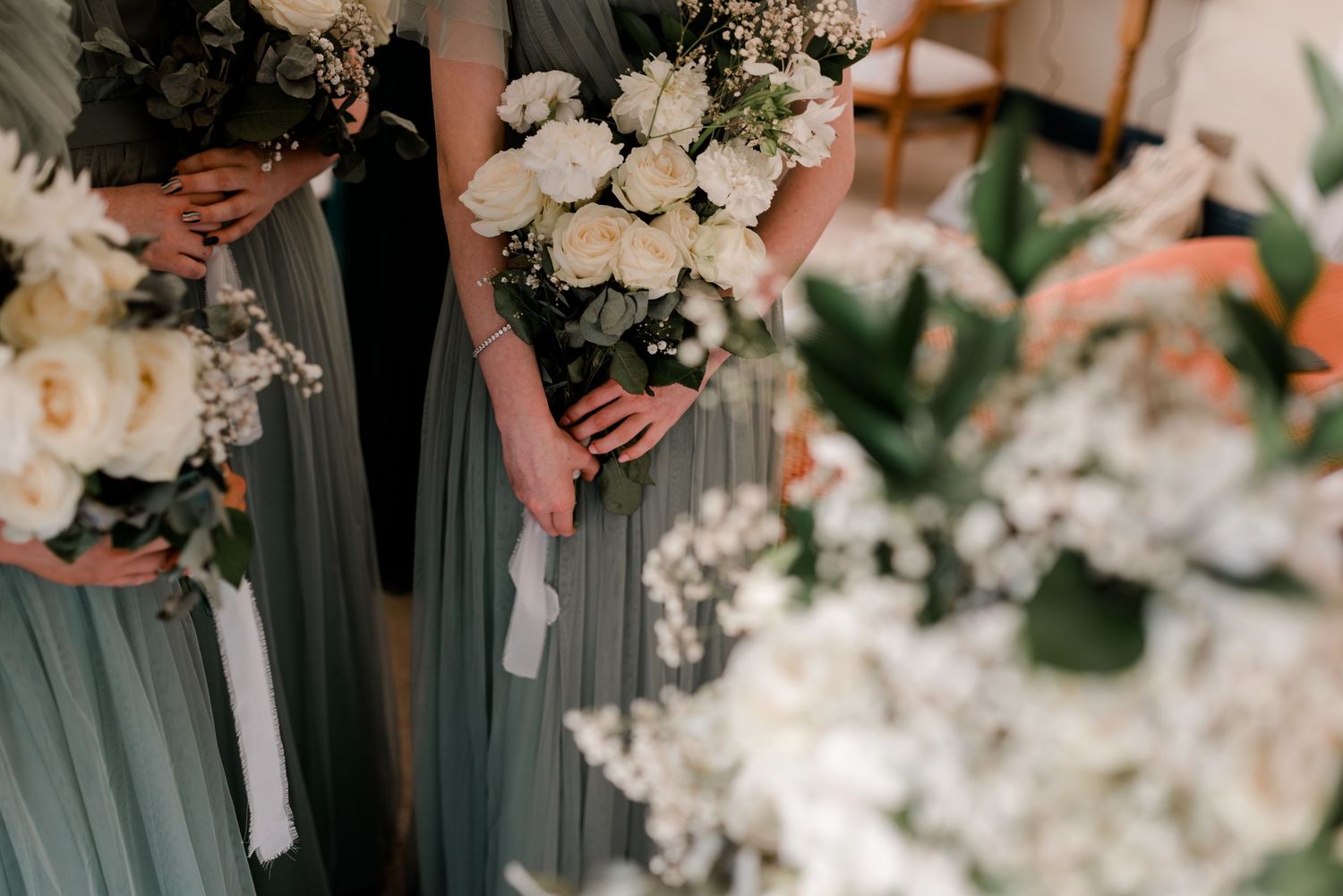 Bridesmaids in sage green dresses holding white floral bouquets at a wedding ceremony.