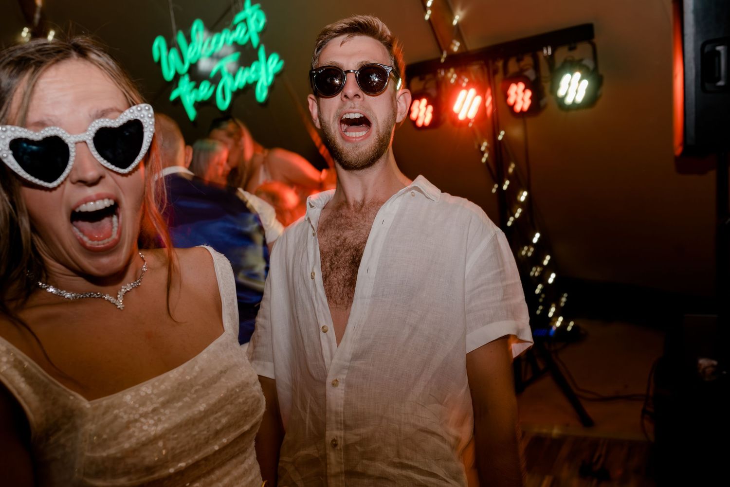 Wedding party celebrating on dance floor with neon lights and festive atmosphere.