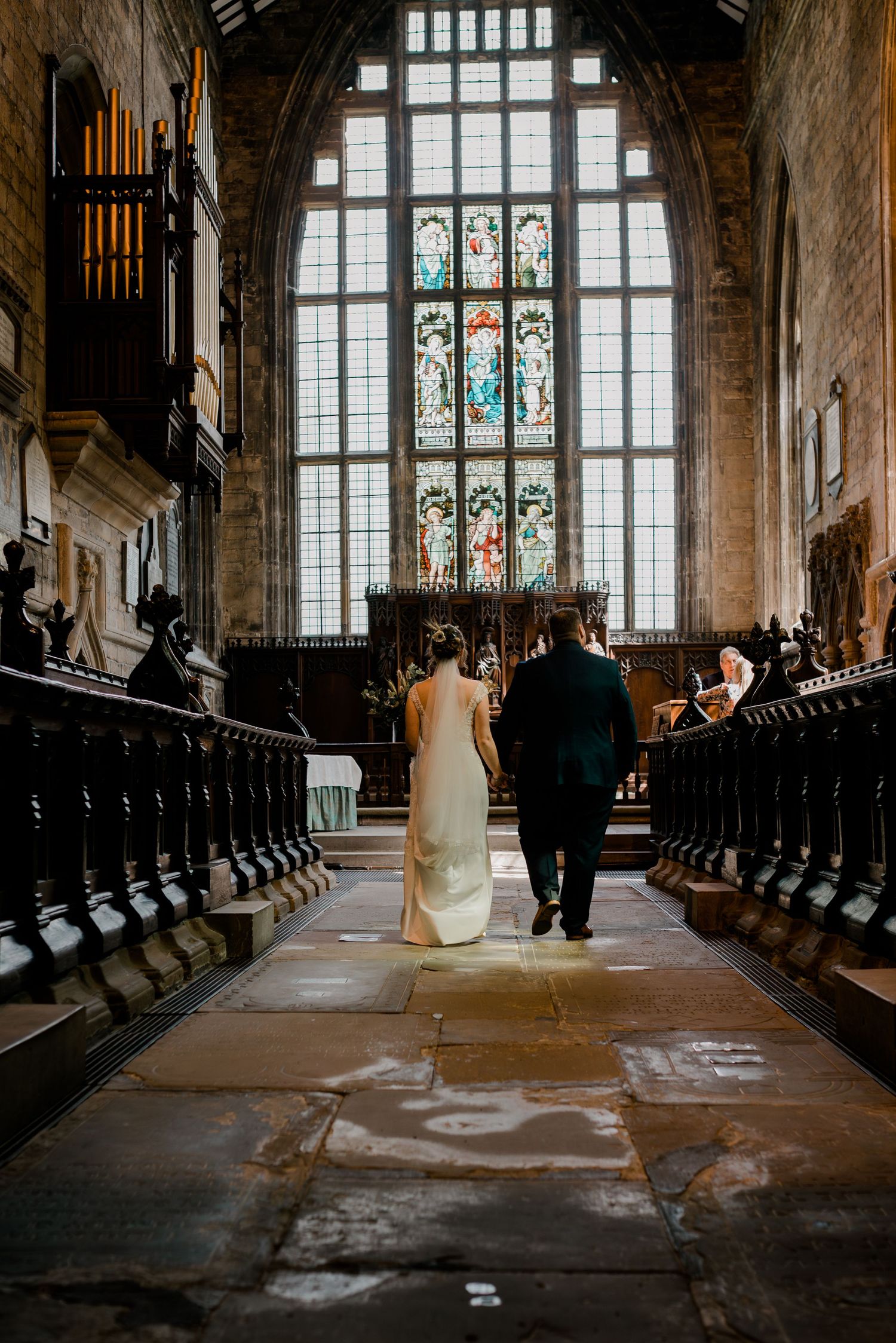 Wedding ceremony in a historic church with dramatic lighting streaming through stained glass windows and wooden pews.