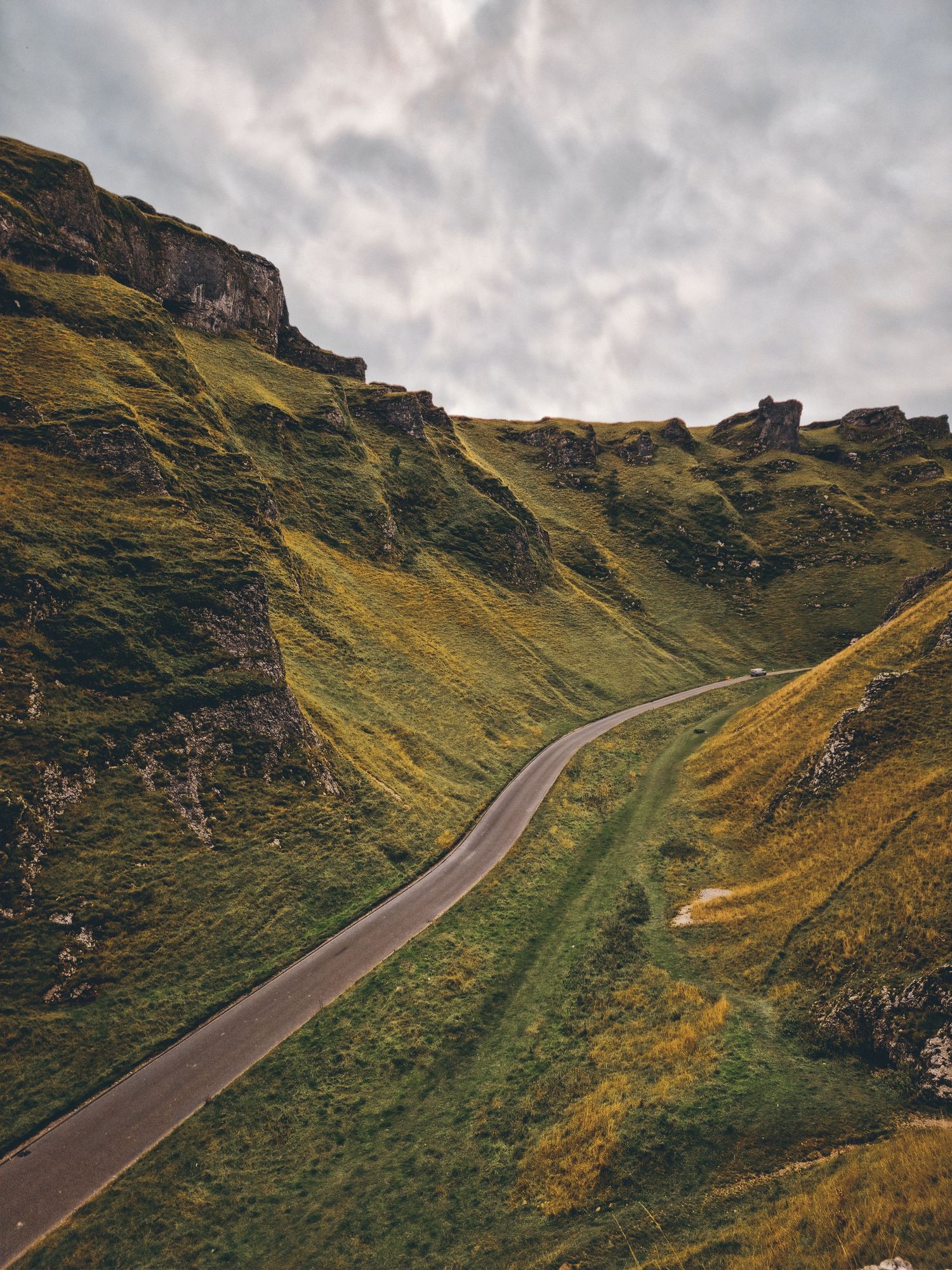 Winding mountain road curves through dramatic Scottish highlands under moody cloudy skies.