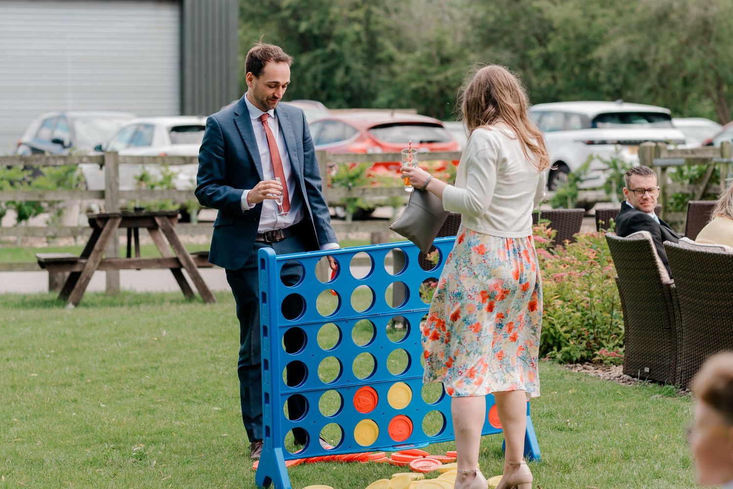 Man and woman playing giant Connect Four game outdoors at a garden party event on a sunny day.