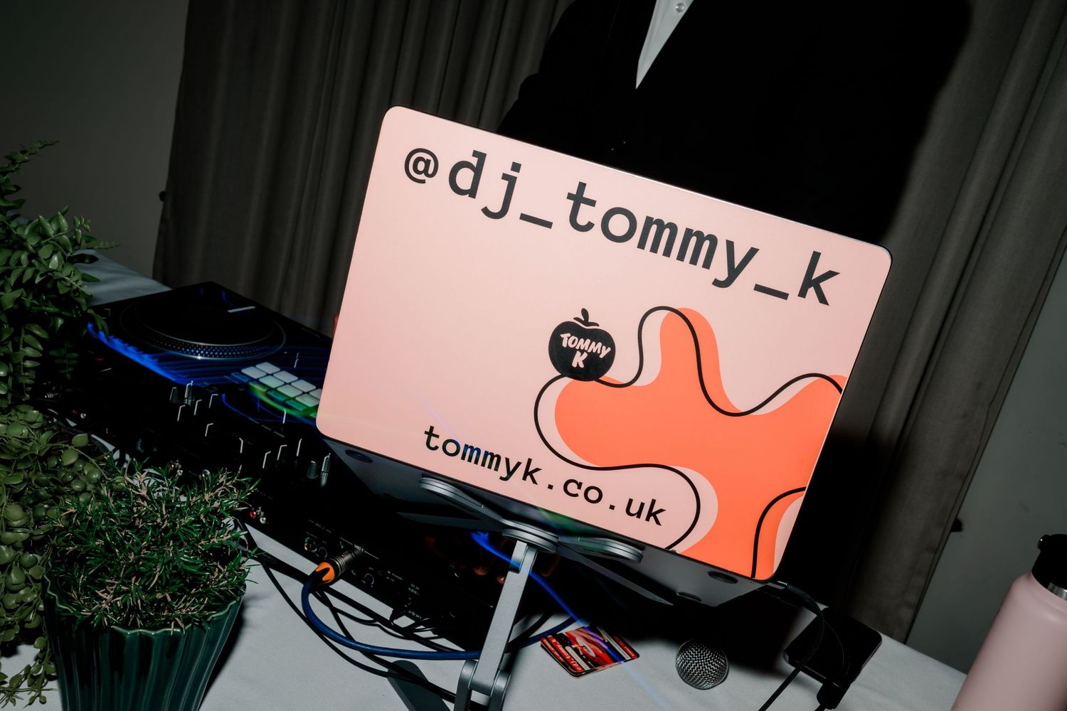 DJ Tommy K laptop with custom branded sticker showing @dj_tommy_k handle and tommyk.co.uk website at live event.