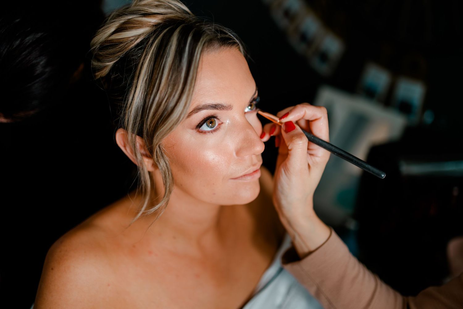 Bride getting makeup applied with a brush during wedding preparations.