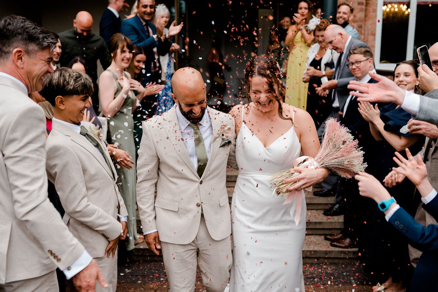 Wedding guests celebrate by throwing confetti during an outdoor celebration.