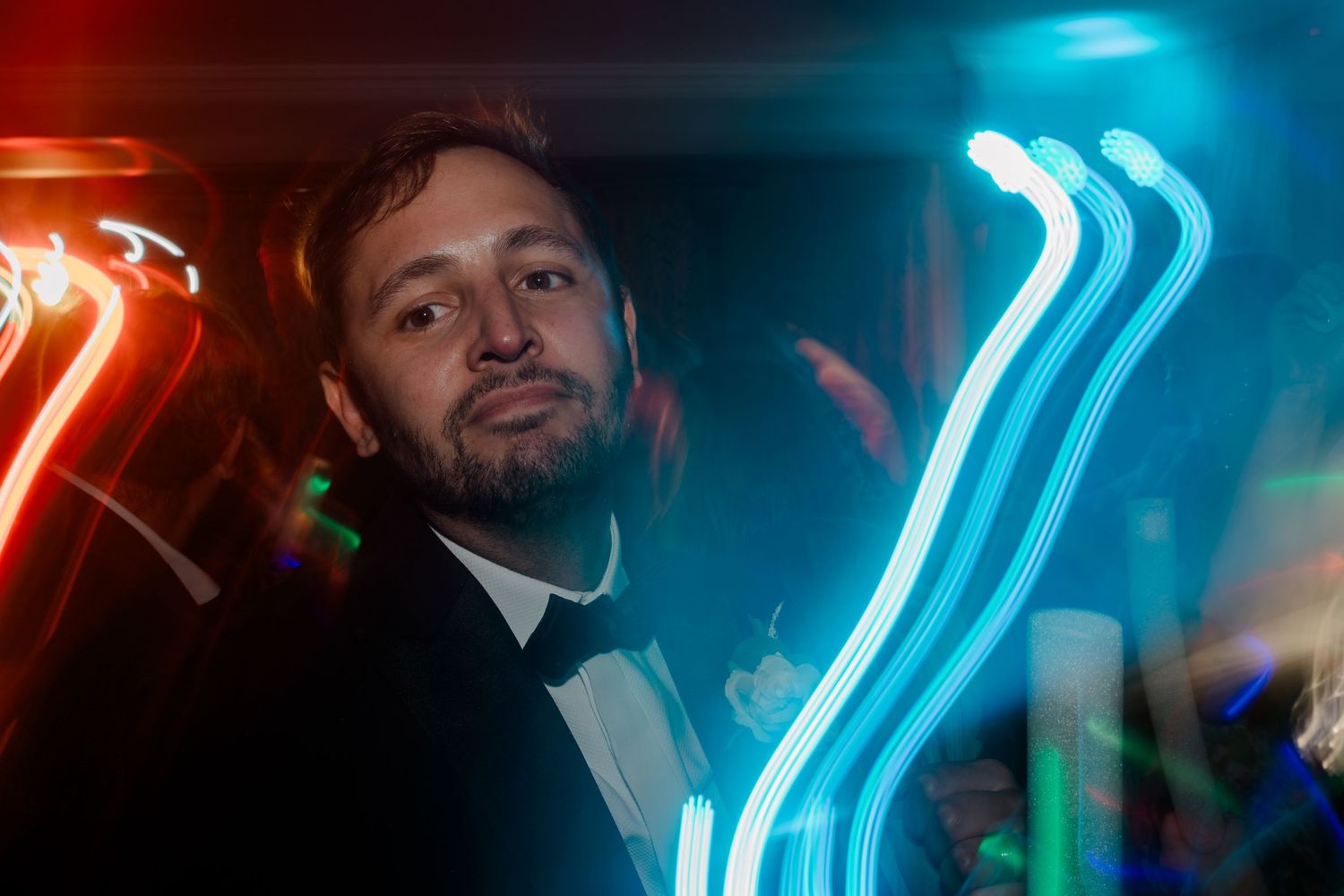 Neon blue lights illuminate a dark nightclub interior with people dancing and socializing in the background.