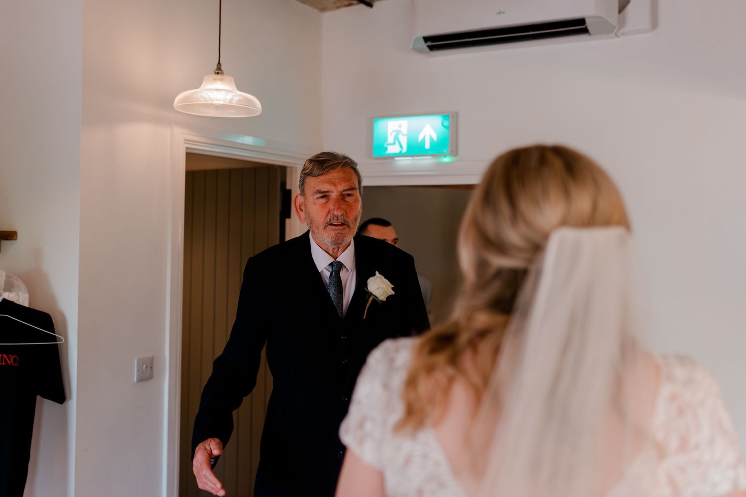 Wedding guests seated in bright modern venue with white decor and pendant lighting.