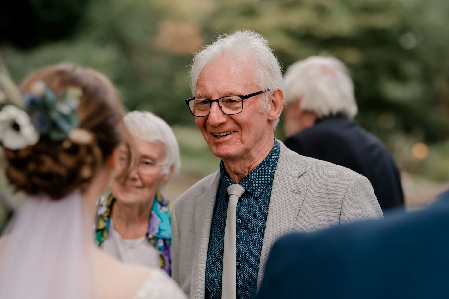 Wedding guests in formal attire gather outdoors during a summer celebration.