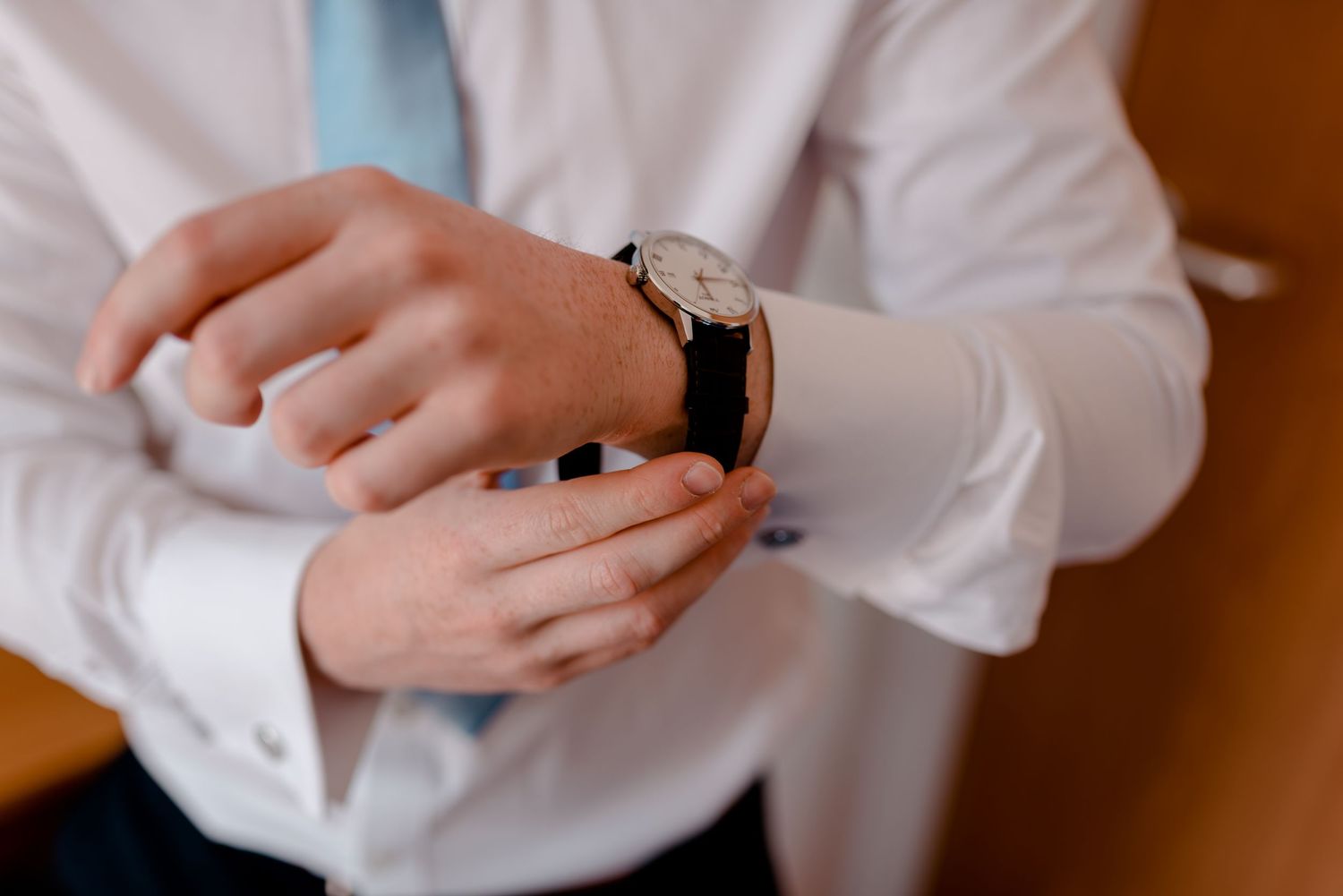 Person wearing white button down shirt adjusts timepiece on wrist in elegant fashion.