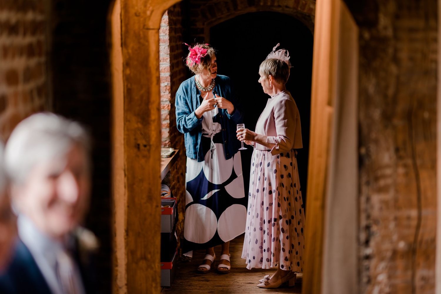 Two wedding guests chat in a doorway of historic brick building.
