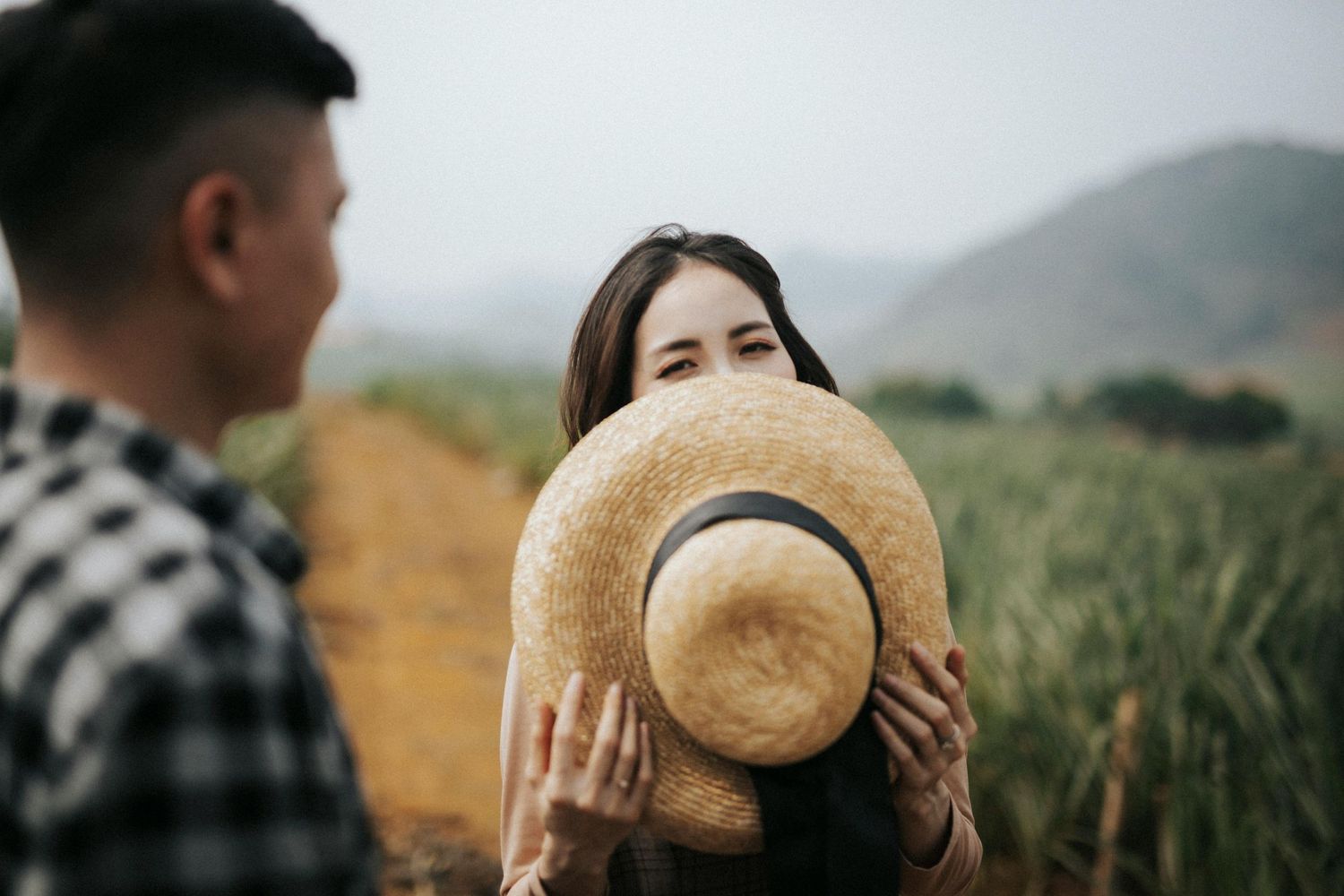 Playful moment in a field with straw hat covering between two people.
