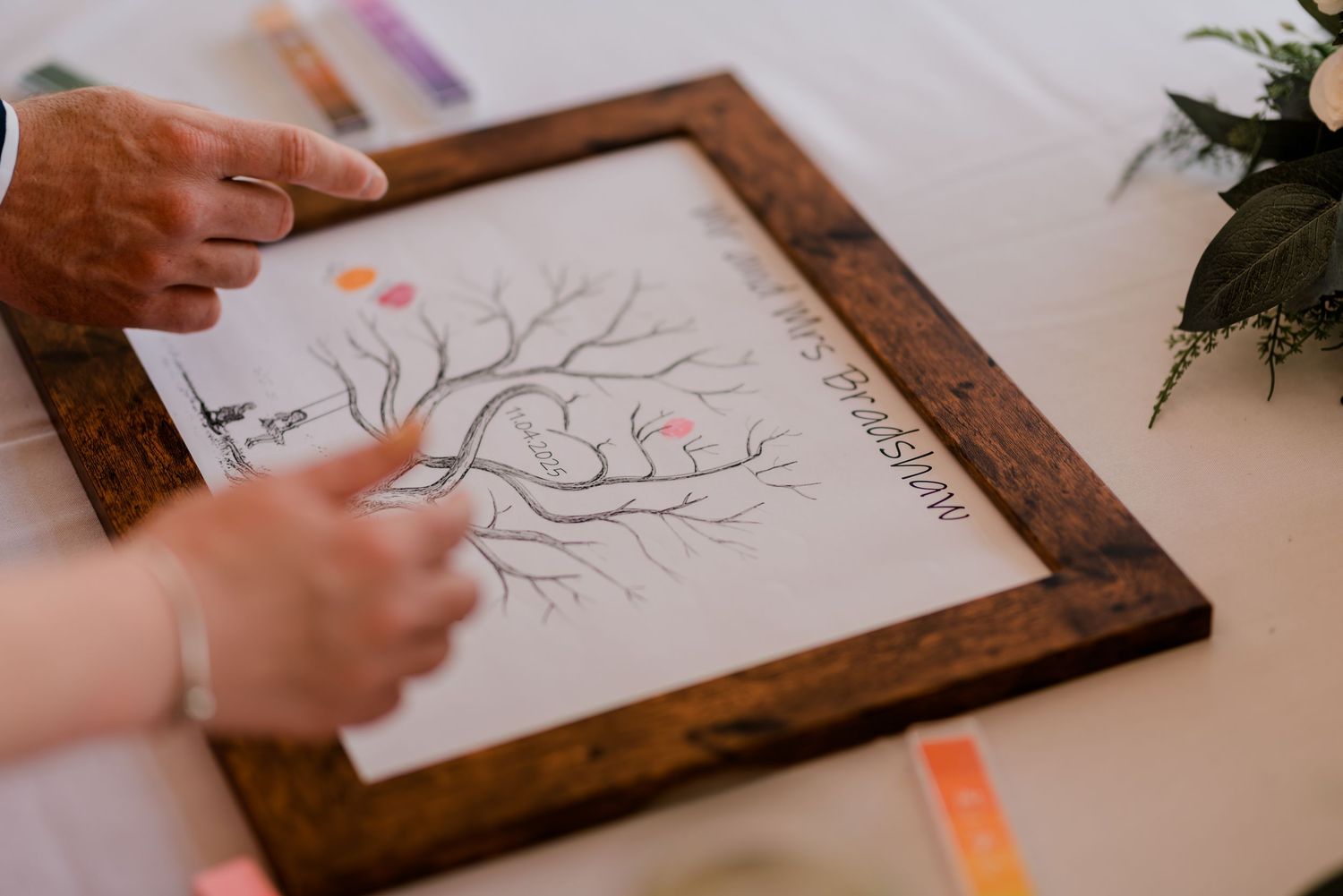 Person holding marker while drawing tree branches and leaves on framed paper with orange accents.