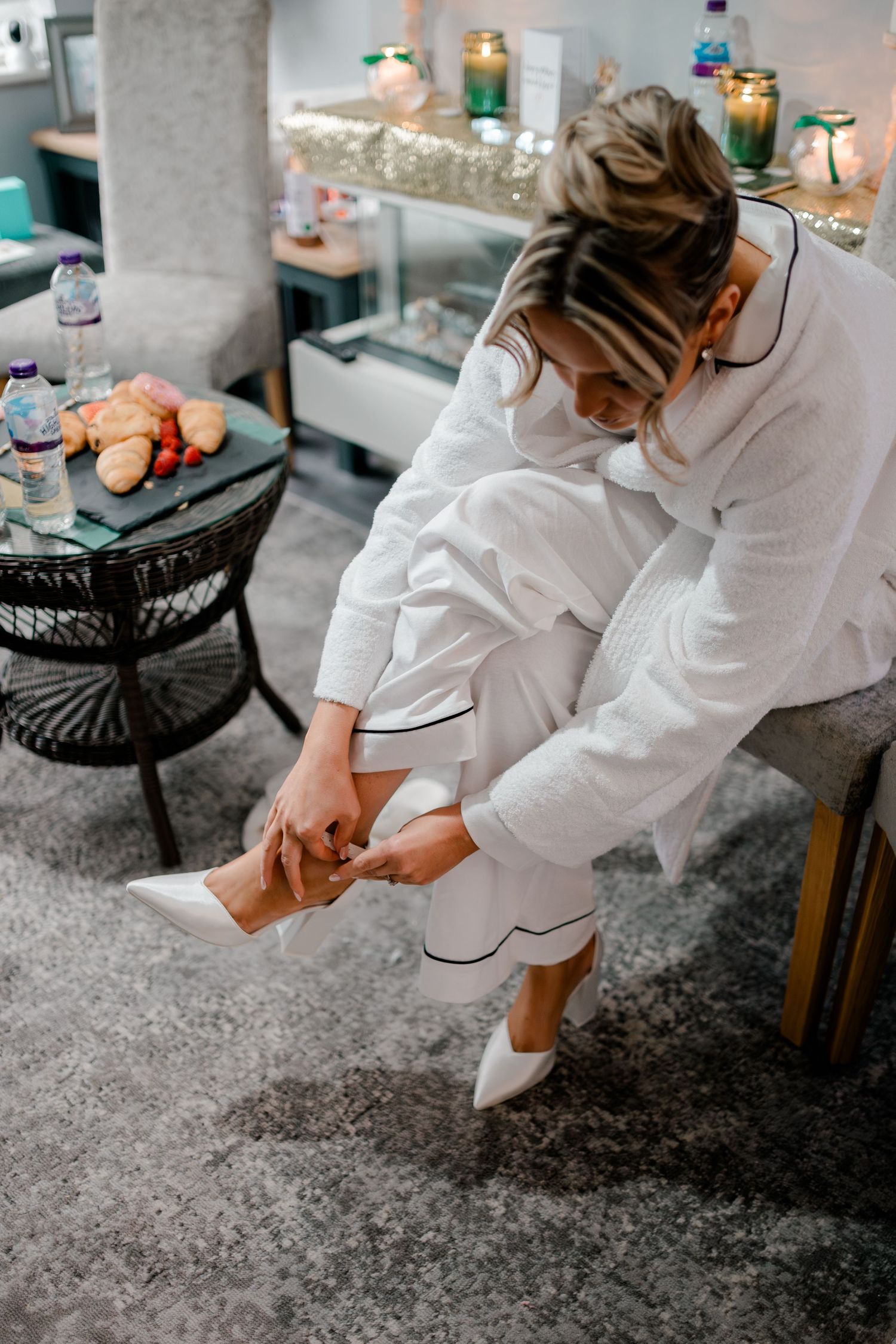 Bride in white pajamas putting on white heels before wedding ceremony.