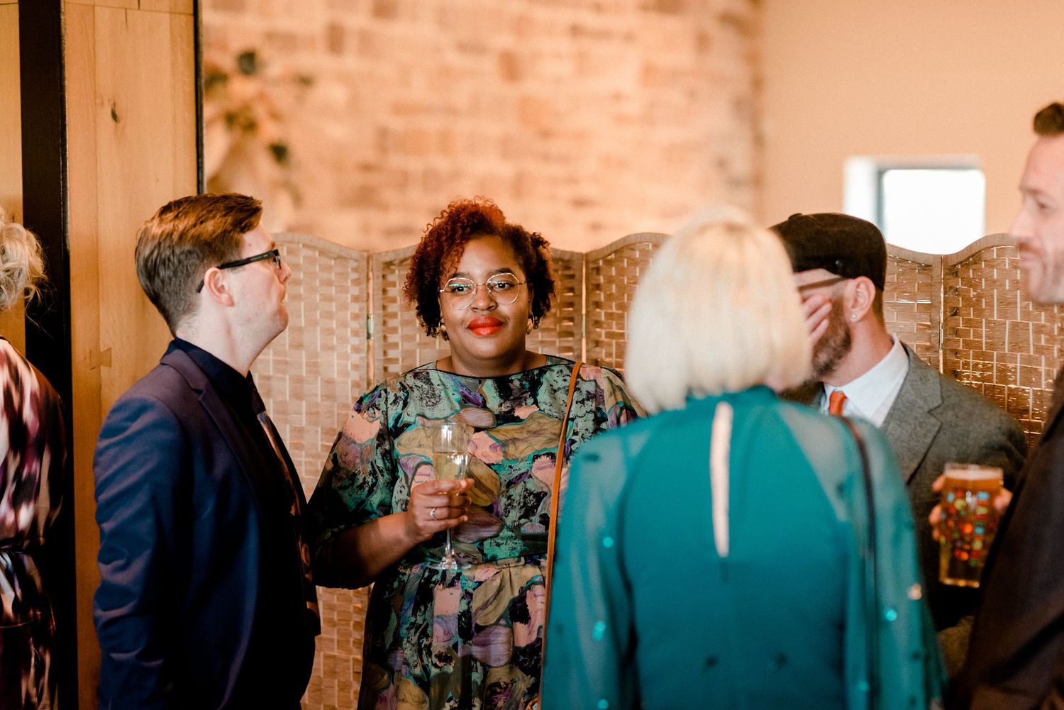 Guests engage in lively conversation during a wedding reception in a rustic brick venue.