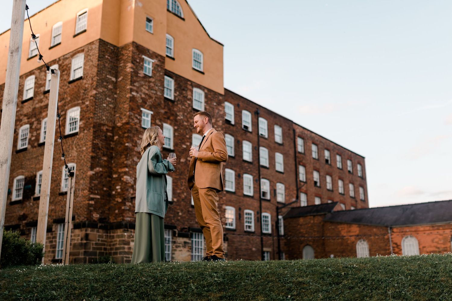 Historic brick apartment building with statue on grassy slope against blue sky.