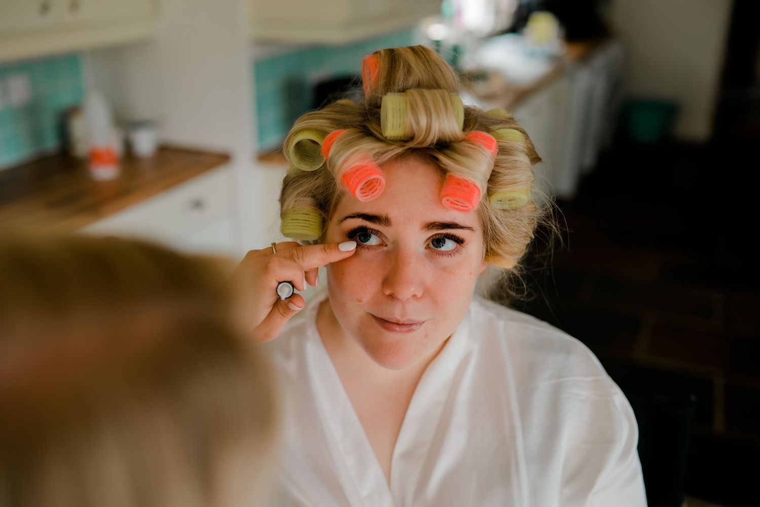Bride getting ready for wedding day with hair in curlers while having makeup applied.