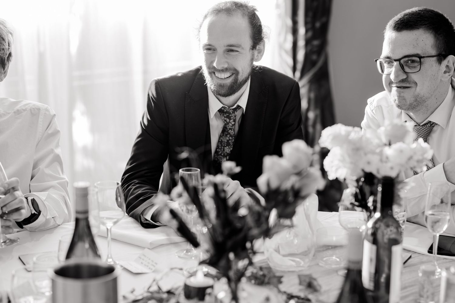 Black and white photo of wedding guests sharing laughter at a reception table.