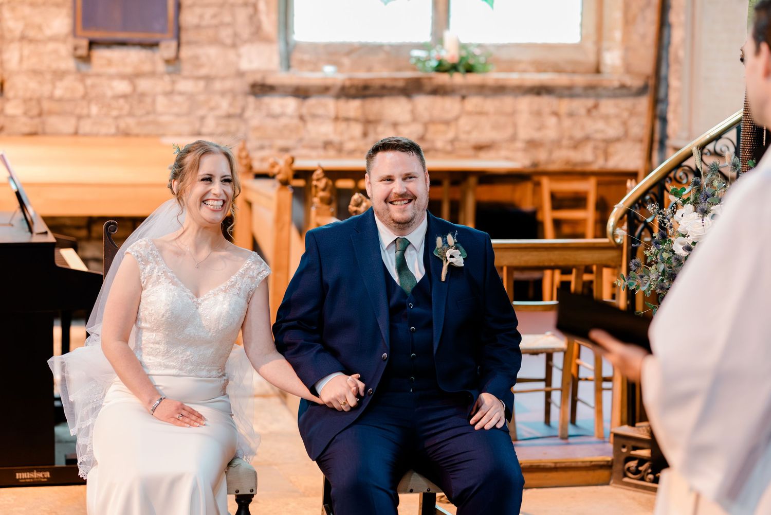 A couple in wedding attire walks down a rustic brick hallway with exposed wooden beams and natural lighting.