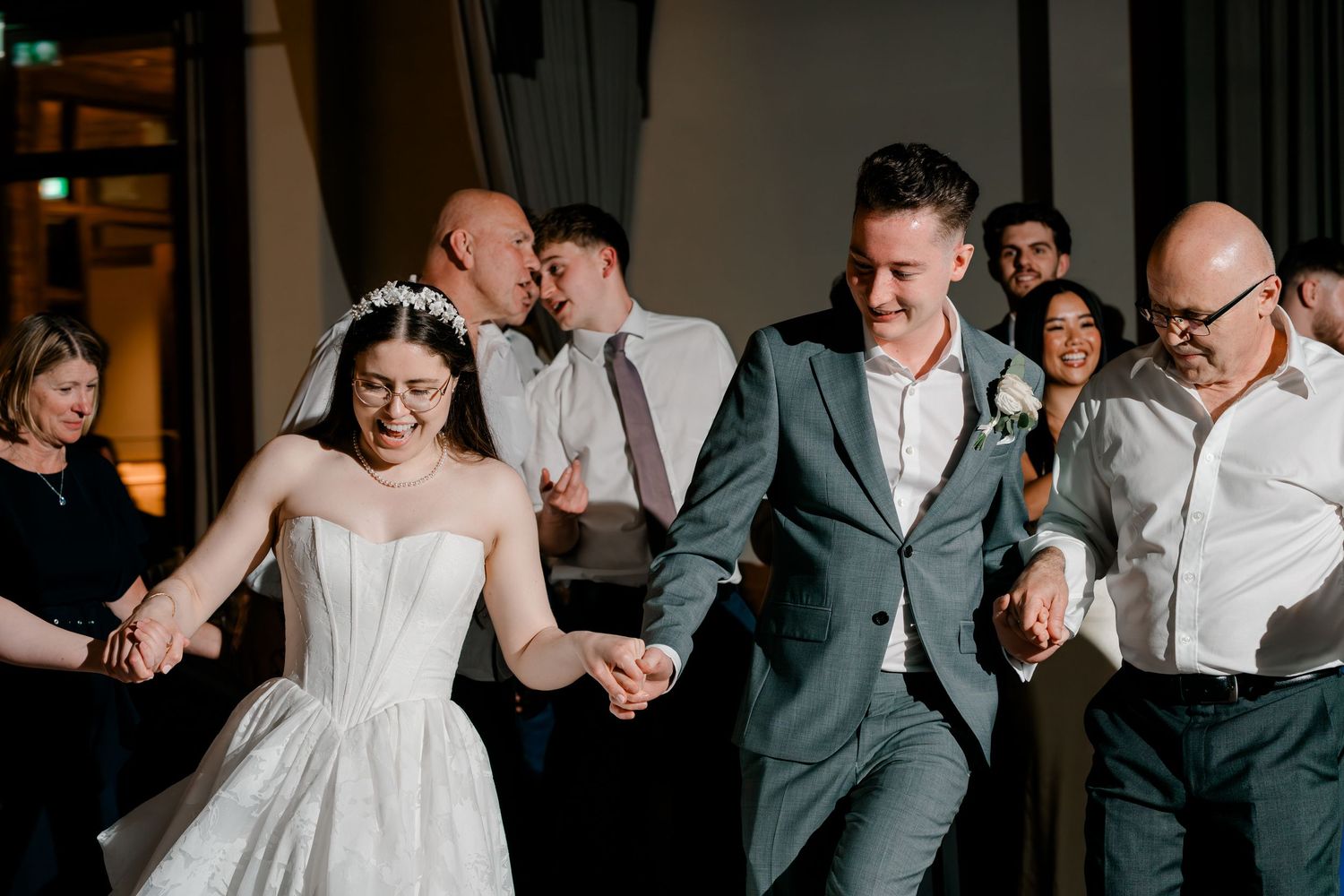 Bride and groom laugh and dance with wedding guests during lively reception celebration.