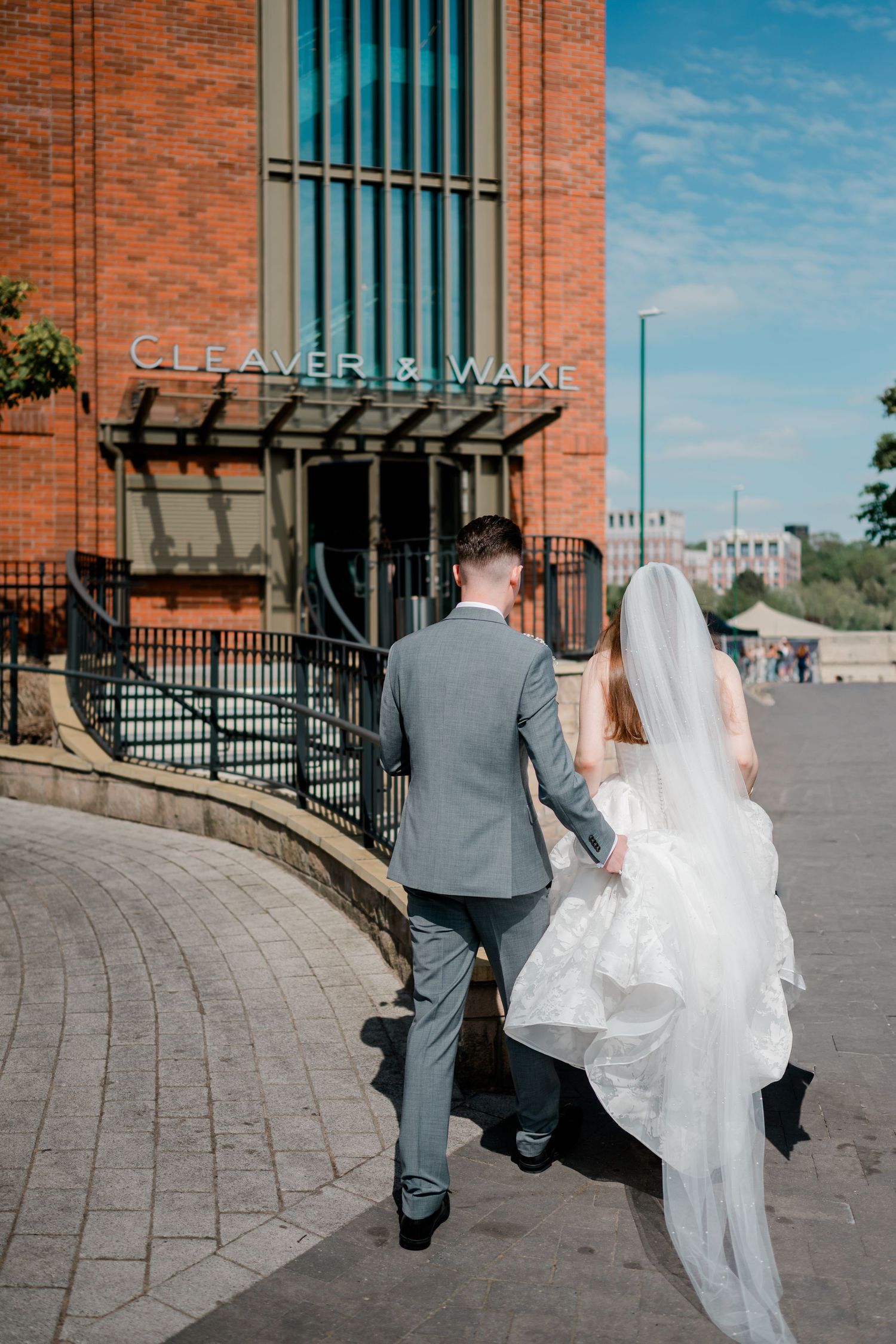 A bride and groom walk hand in hand toward Cleaver & Wake venue on their wedding day.