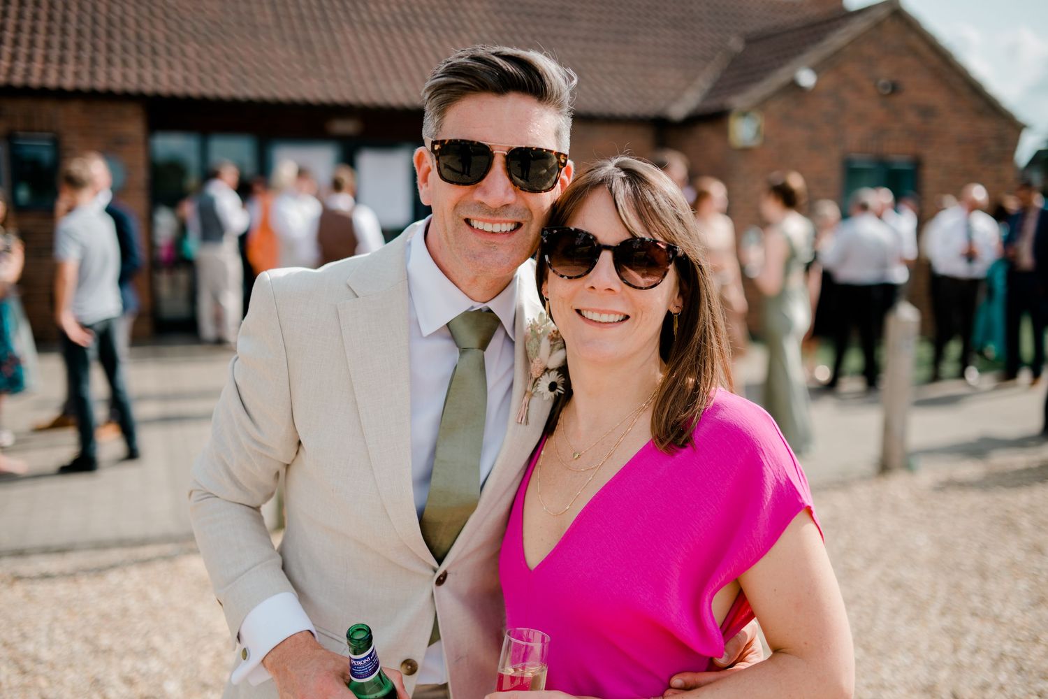 Wedding guests gathered on a gravel courtyard outside a brick building on a sunny day.