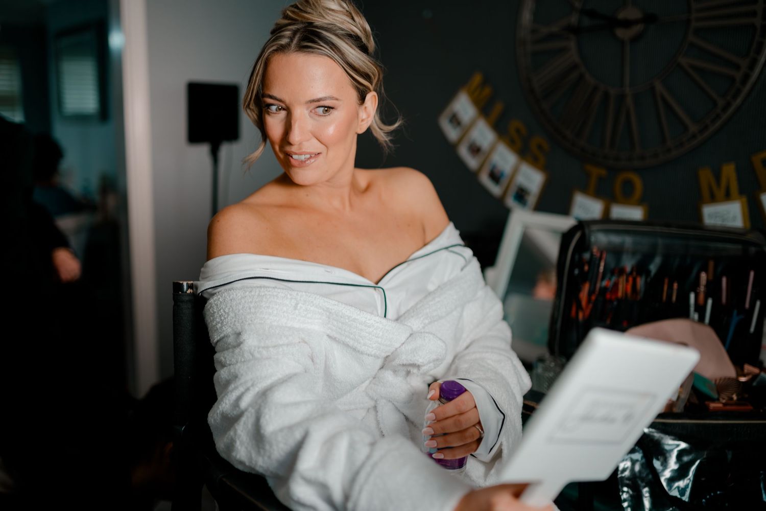 Smiling bride in white robe reading a card during wedding preparations.